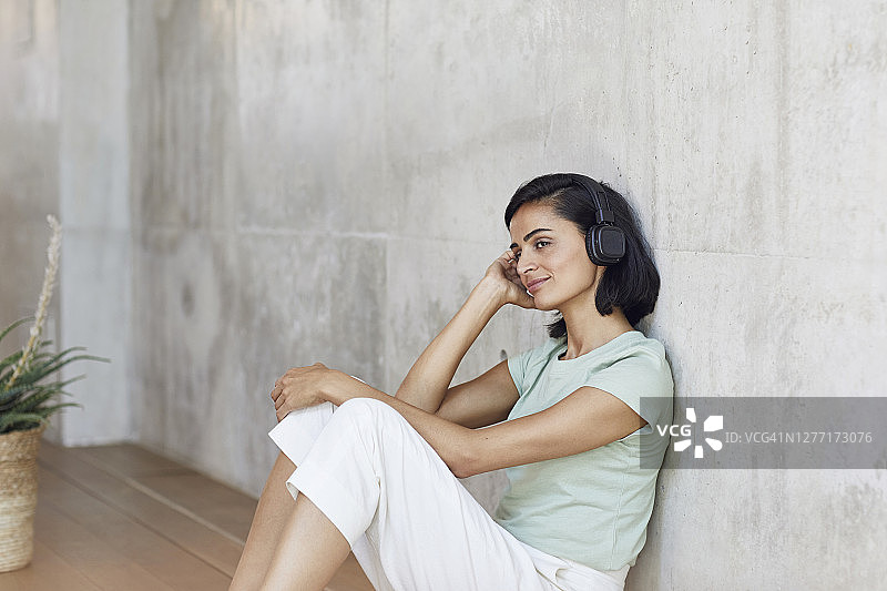 在办公室靠墙坐着，戴着耳机听音乐的深思熟虑的女商人图片素材