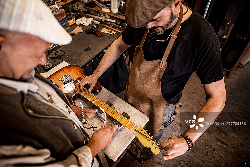 木匠正在制作吉他，而顾客在手表和等待图片素材
