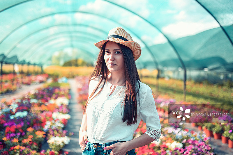 戴着帽子的微笑女人，站在温室的鲜花中图片素材