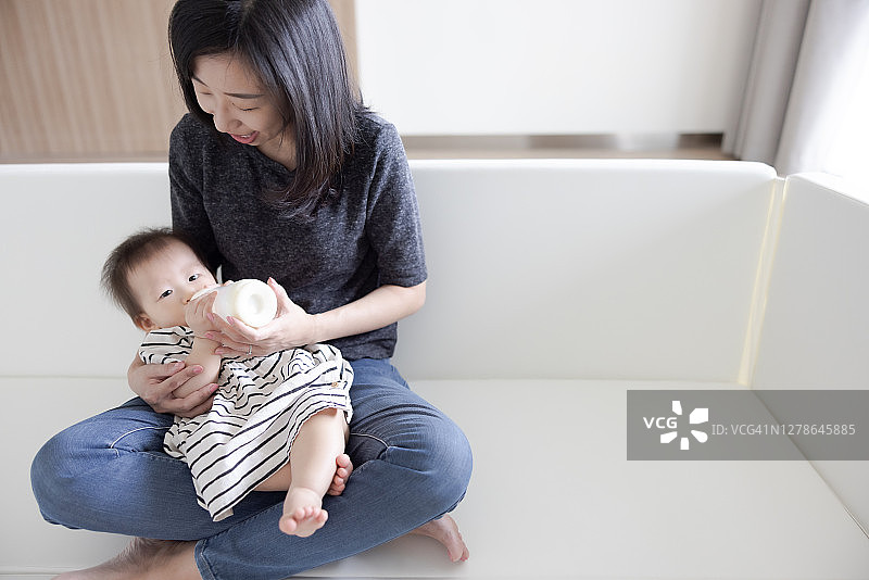 可爱的亚洲宝宝喜欢妈妈膝上的奶瓶图片素材