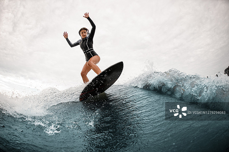 一名年轻女子站在冲浪板上，积极地在波浪上保持平衡图片素材