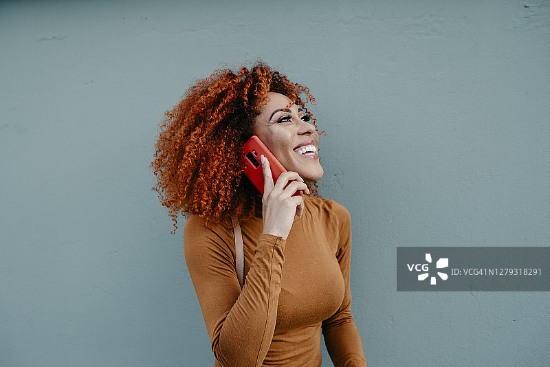 一个愉快的年轻女子，留着非洲式发型，靠墙站着打电话图片素材