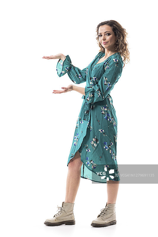 快乐自信的年轻时尚的女人在花裙子呈现双手在复印空间。图片素材