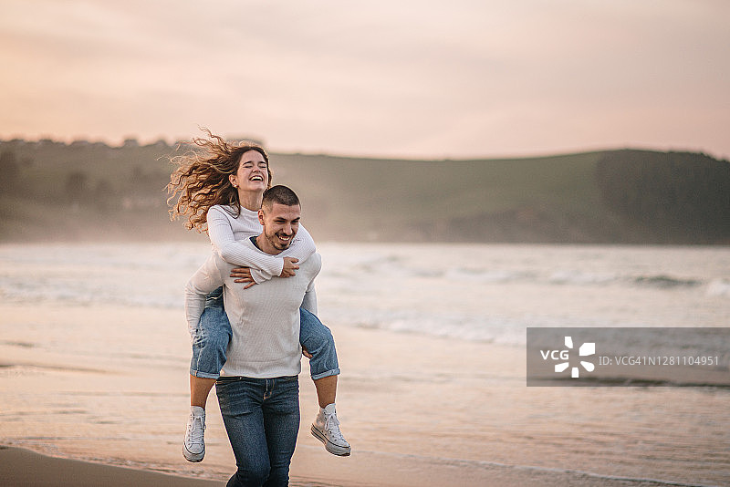 日落时分，一对年轻夫妇在海滩上背着背包散步图片素材