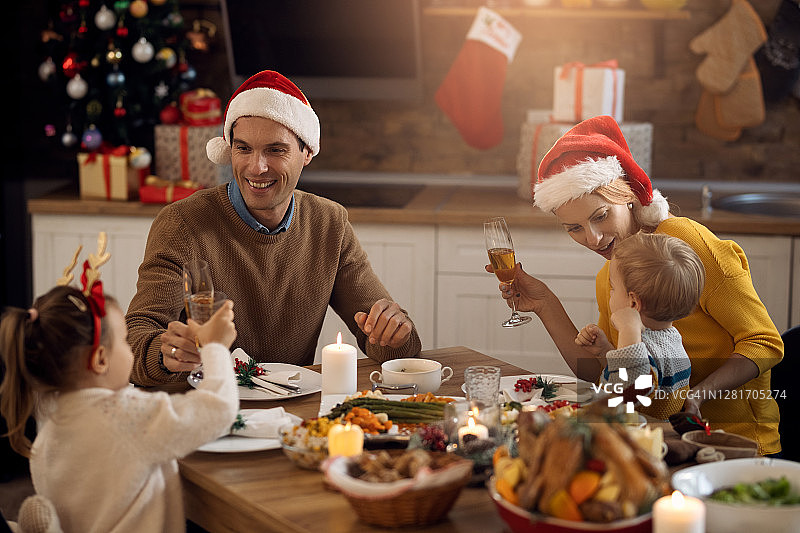 快乐的父母和他们的小孩在餐桌上享受圣诞午餐。图片素材