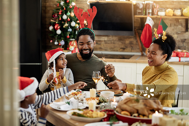快乐的黑人家庭在圣诞午餐期间在餐厅玩烟花。图片素材