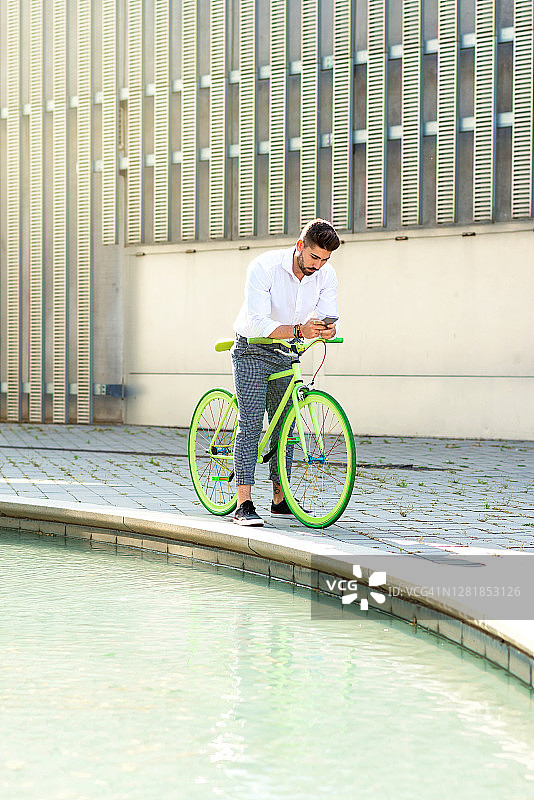 户外肖像英俊的年轻人用手机和固定齿轮自行车在街上。图片素材