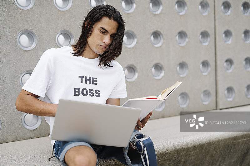 一个戴着假肢的年轻人靠墙坐着用笔记本电脑工作图片素材
