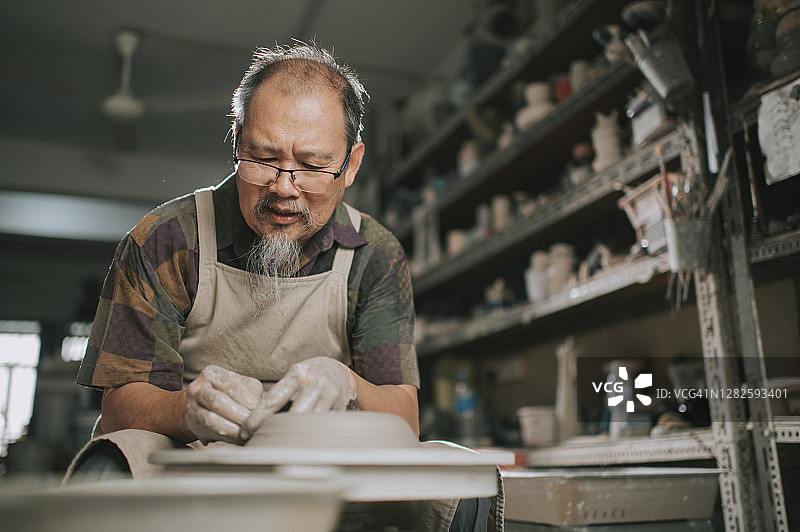 亚洲华人高级泥塑艺术家在他的工作室与纺织陶轮工作图片素材