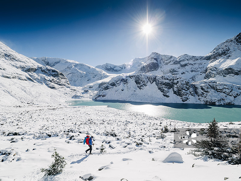 一个孤独的山地徒步者走过一片明亮的、白雪覆盖的景观，背景是高山湖泊和冰川覆盖的山脉图片素材
