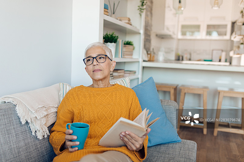 年长的女人在沙发上悠闲地喝着咖啡和看书图片素材