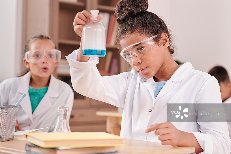 两个戴眼镜、穿白大褂的女学生在看蓝色的液体物质图片素材