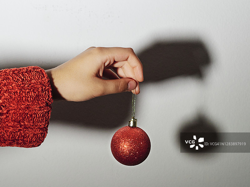 手里拿着一个红色的圣诞球，背景是白色的墙图片素材