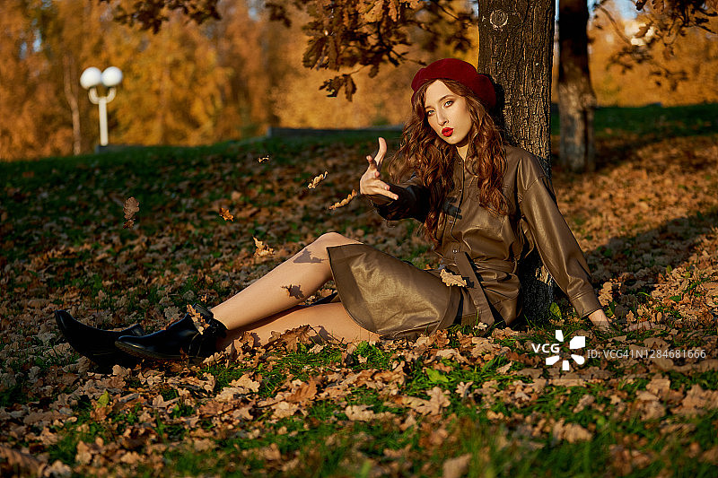 一个女人在秋天的肖像帽子贝雷帽和雨衣附近的一棵树在秋天黄色的树叶图片素材