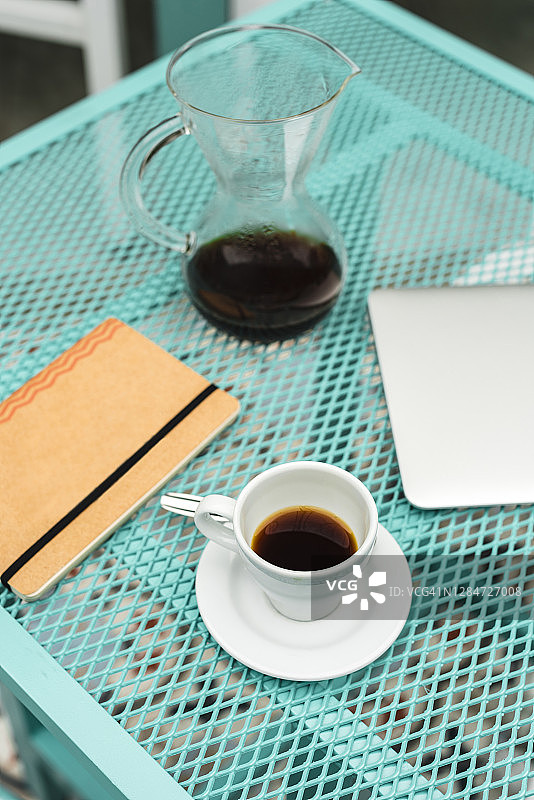 笔记本电脑，笔记本电脑，咖啡杯和茶壶放在咖啡馆的桌子上图片素材