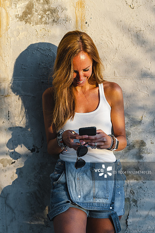 面带微笑的女人靠墙站着用手机图片素材