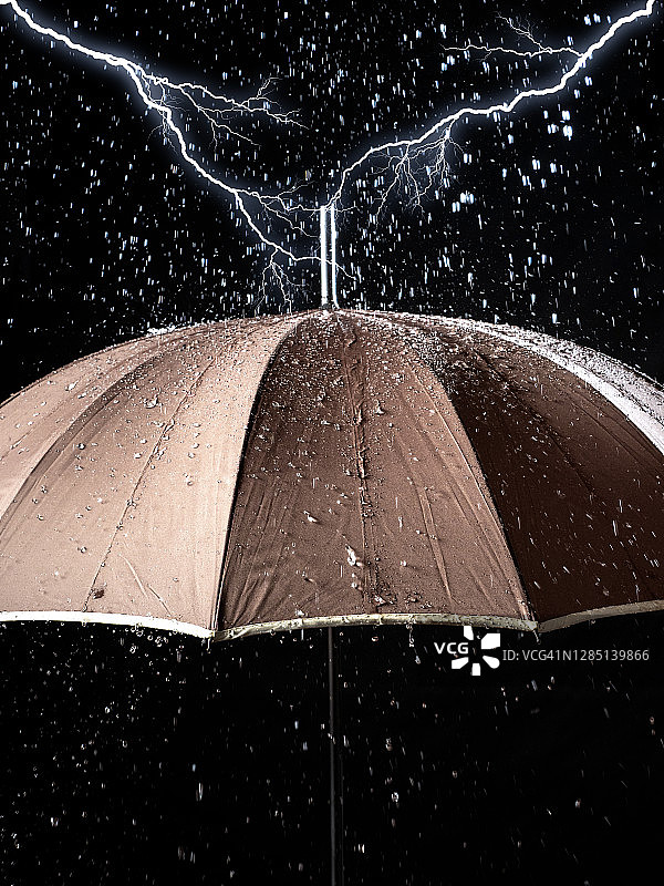雨滴和闪电落在黑色背景上的雨伞上。图片素材