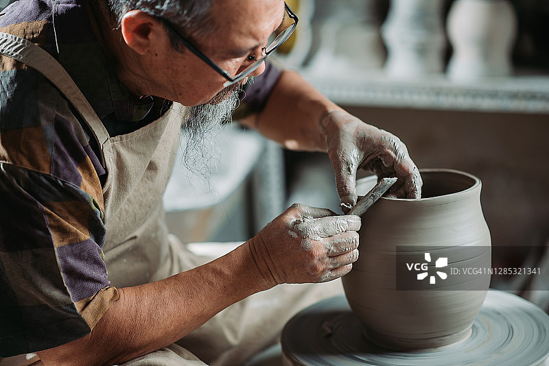 亚洲华人高级陶艺师在他的工艺工作室里，在一个旋转的陶轮上制作陶器图片素材