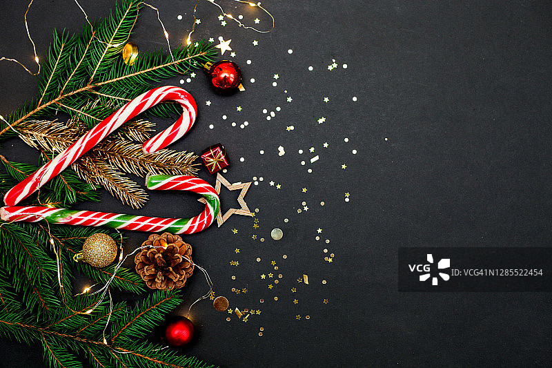 圣诞贺卡:用牛皮纸包装的礼盒，松树枝，松果，装饰品，黑色背景上的金色五彩纸屑。图片素材