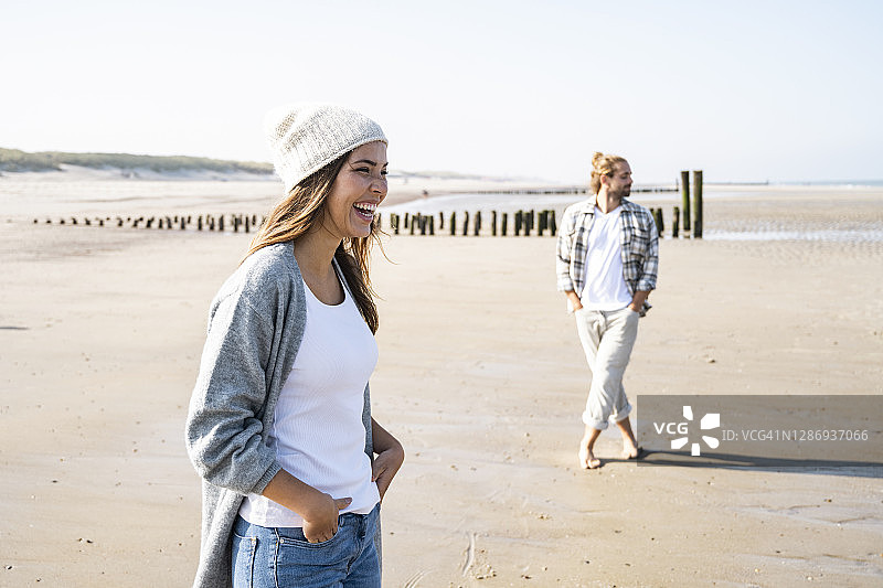在阳光明媚的日子里，一个快乐的年轻女子双手插在口袋里站在海滩上图片素材