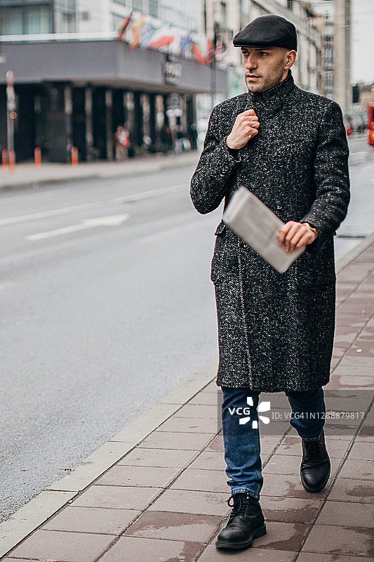 英俊的年轻人穿着温暖的现代外套走在城市的街道上图片素材