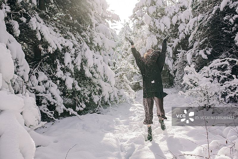 一个年轻的女人在一个美丽的冬天的森林里，杉树覆盖着雪。图片素材