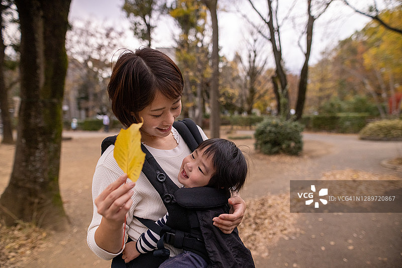 一个年轻的女人和她的小男孩在公园里玩黄叶图片素材