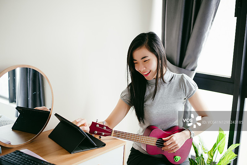 年轻的亚洲女人在她的房间玩尤克里里琴。图片素材