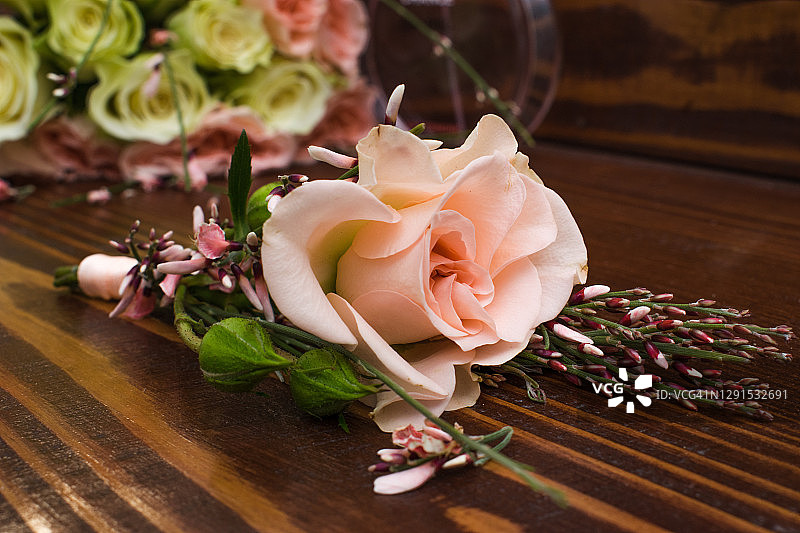 棕色木桌上放着一束金龟子、白玫瑰和粉红玫瑰，还有新郎的胸花图片素材