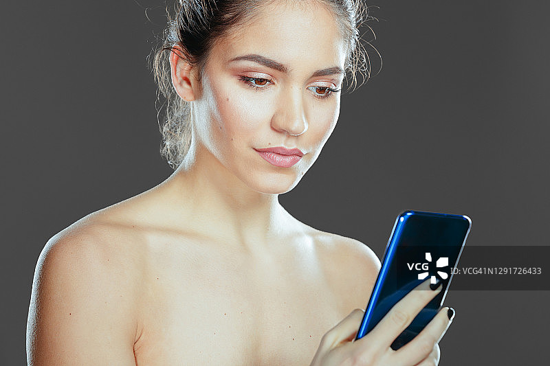 美丽的年轻女子裸体看智能手机的肖像图片素材