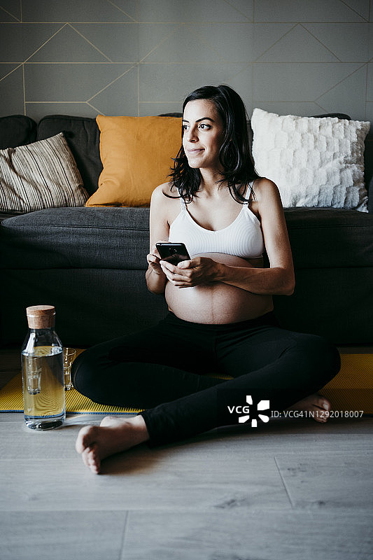 体贴的孕妇坐在客厅里拿着手机图片素材
