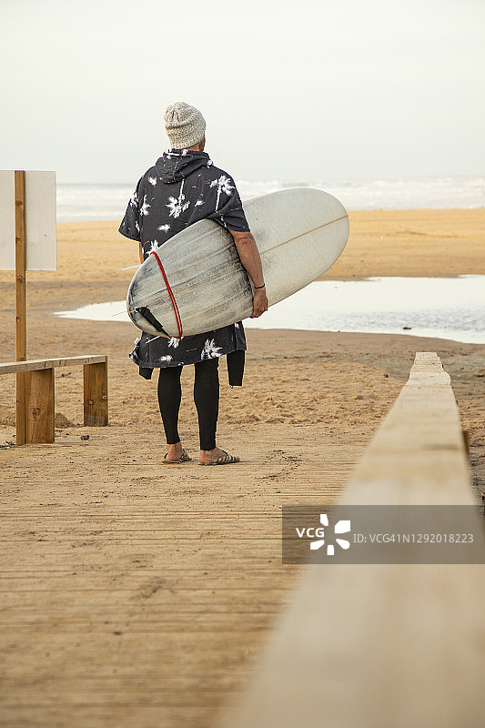 男性冲浪者拿着冲浪板站在海滩的木板路上图片素材