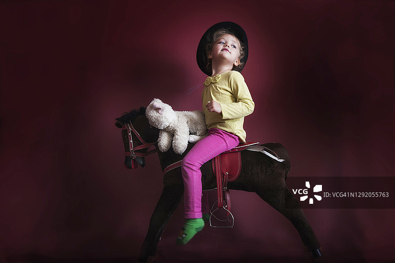 一个女孩和她的泰迪熊骑在摇摆木马上的肖像图片素材