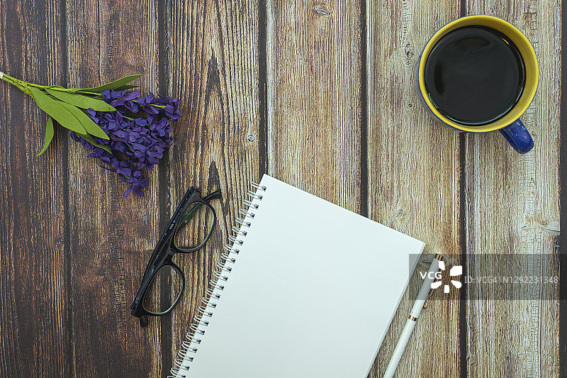 木桌上放着空白记事本，上面放着玻璃杯、咖啡杯和鲜花。概念和背景。图片素材