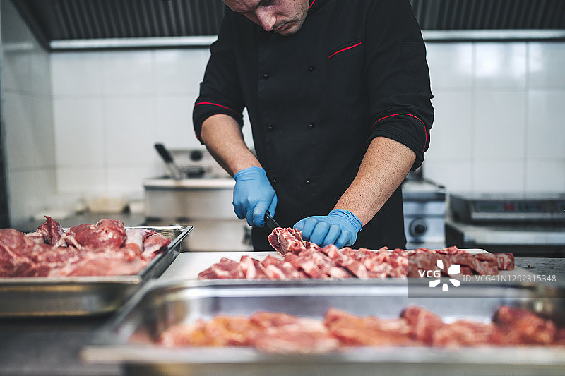 男屠夫在餐厅厨房用锋利的刀切生肉图片素材