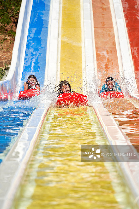 三个孩子在水上乐园玩滑梯。图片素材