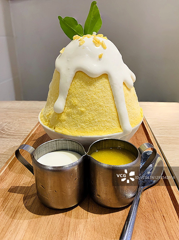 “Kakigori”的字面意思是“刨冰”，这是一种日式甜点，配上小罐子里的芒果糖浆和椰奶。芒果卡戈里上面放着椰奶和酥脆的黄豆放在木盘上。图片素材