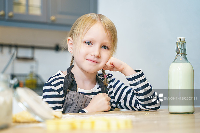 一个可爱的小女孩在厨房里围着围裙准备做饼干的面团图片素材