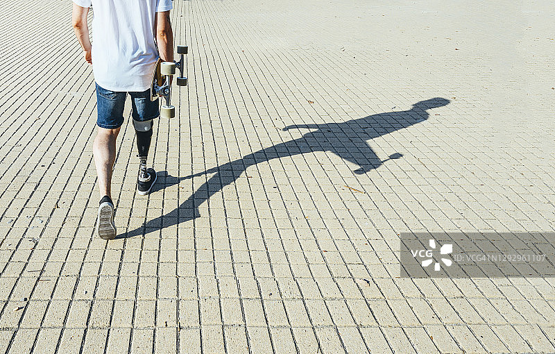 一个年轻人带着假肢走着，拿着滑板图片素材