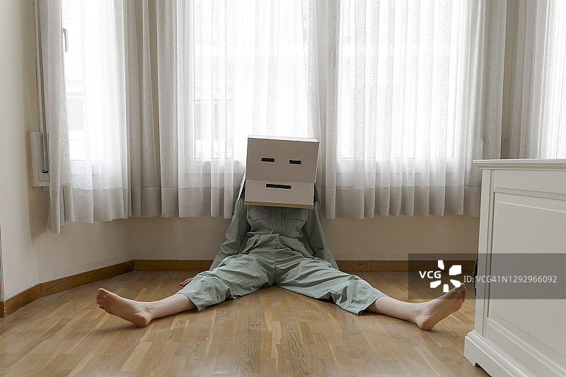 一个女人头上戴着一个纸盒，脸上带着无聊的笑脸坐在地板上图片素材