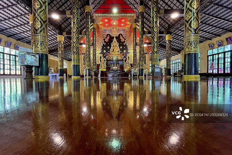 Wat Khao Banchop Temple木质礼拜堂美丽的内部，里面有沉思中的金色佛像和地板上美丽的倒影。图片素材