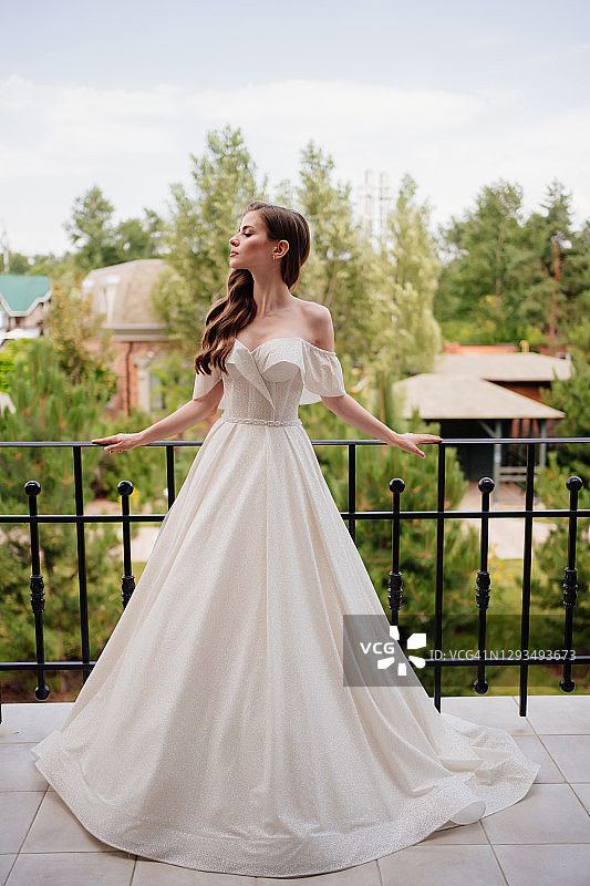 一位穿着白色婚纱的美丽年轻女子站在阳台上。图片素材