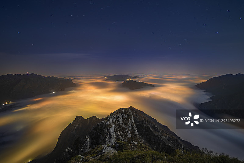 从意大利伦巴第莱科省科尔蒂尼奥内山顶俯瞰莱科市的灯光映照下的雾堤图片素材
