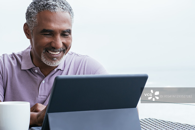 微笑的男子坐在阳台上看数字平板电脑图片素材