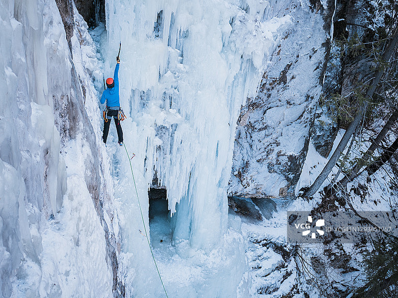 在不列颠哥伦比亚省的内陆，一名男性冰上攀登者正在攀爬一个高高的、垂直的冰冻瀑布图片素材
