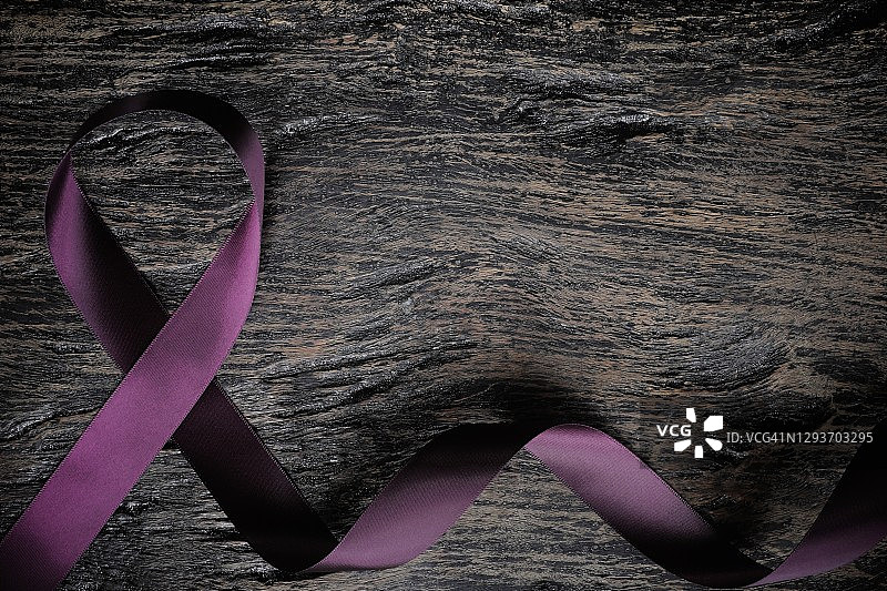 俯视图的紫色丝带在木材背景与复制空间。胰腺癌、癫痫、平滑肌肉瘤、狼疮、阿尔茨海默病和囊性纤维化的认识概念。图片素材