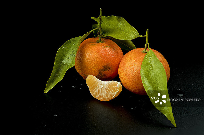 新鲜成熟的橘子，片，绿叶，横截面黑色背景。图片素材