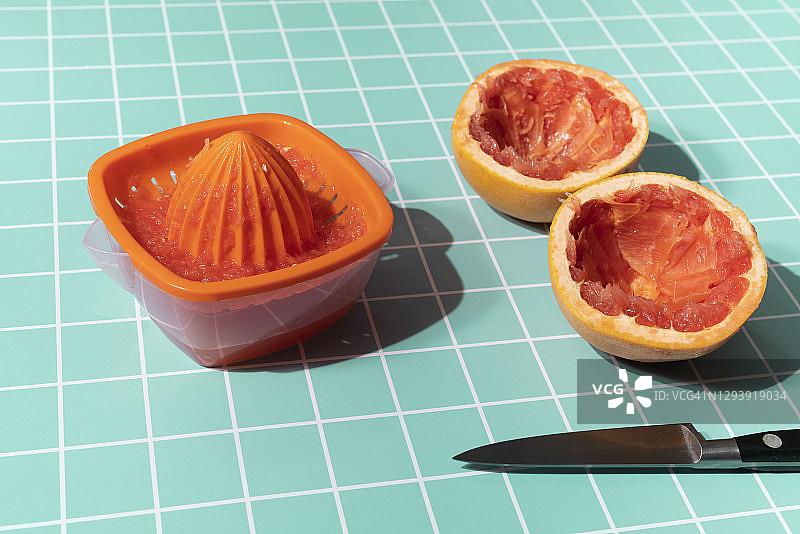 桌子上两个半个柚子，一个橙子榨汁机和一把绿松石色的小刀图片素材