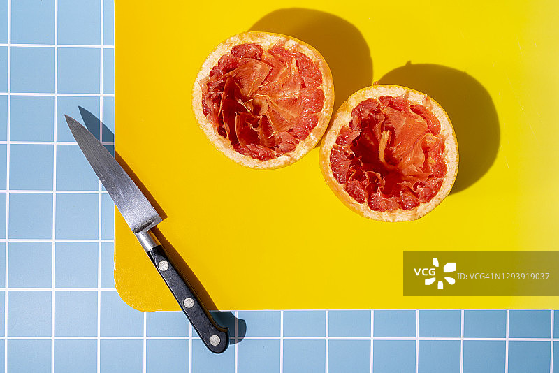 在切菜板上切成两半的葡萄柚和蓝色背景上的小刀图片素材