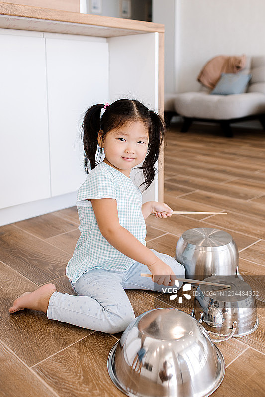 一个亚洲小女孩坐在厨房里像打鼓一样打锅图片素材